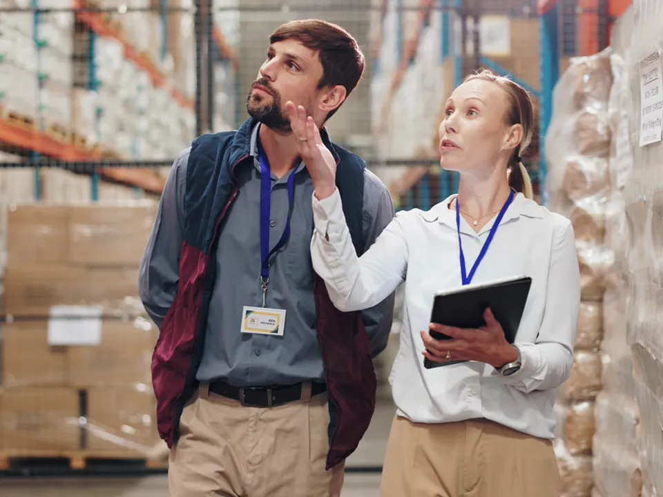 Two people walking and talking between high-bay racks in a warehouse